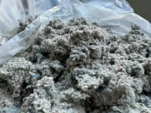 A close-up sample of recycled loose-fill cellulose attic insulation material placed inside a plastic bag.